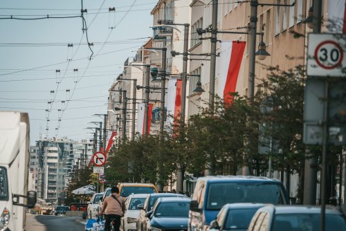 ulica, ruch uliczny. Widoczne latarnie uliczne a na nich flagi Polski