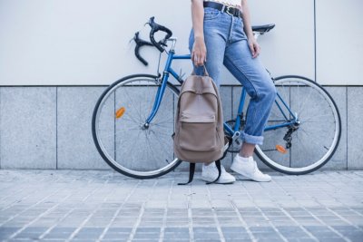 młoda kobieta na tle roweru z plecakiem w ręku - zdjęcie sekcji od pasa w dół