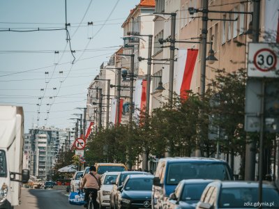 ulica, ruch uliczny. Widoczne latarnie uliczne a na nich flagi Polski