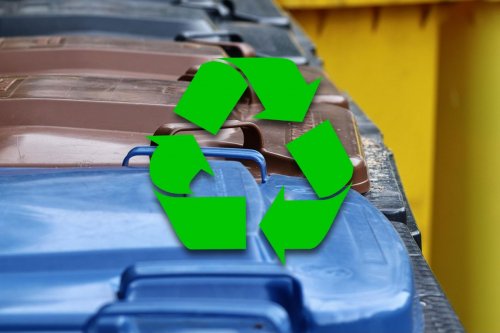 Zdjęcie ilustracyjne. Kolorowe pojemniki na odpady, na pierwszym planie zielony znak ze strzałkami symbolizujący recykling