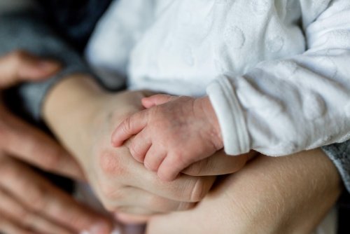 Ręce dorosłej osoby trzymającej dziecko-niemowlę, widoczne ręce niemowlaka, dłonie dorosłego