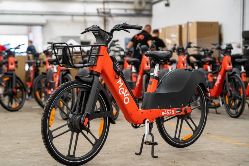 Hala magazynowa, wiele rowerów metropolitalnych Mevo. Na środku stoi jeden rower w kolorze czerwonym, z naklejką Mevo.