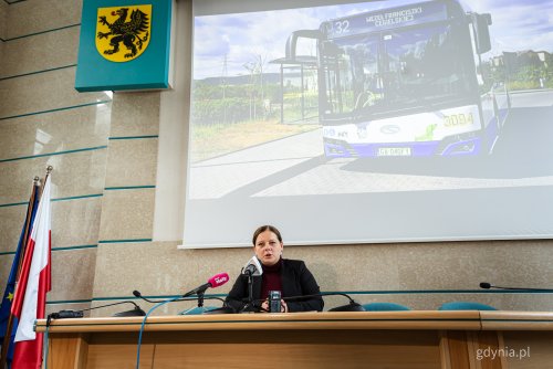 Sala obrad rady miasta, przy stole siedzi Aleksandra Kosiorek, na ekranie w tle wyświetlane zdjęcie gdyńskiego autobusu z napisem 