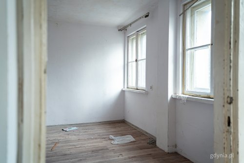 Zdjęcie pustego mieszkania, białe ściany, widoczne dwa okna z podziałką
