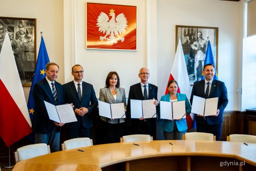Sala w Urzędzie Wojewódzkim, grupa samorządowców stoi przy stole, wszyscy trzymają teczki i pokazują treść listu, w tle godło Polski. Stoją od lewej Mieczysław Struk, Emil Rojek, Mariola Zmudzińska, Bogdan Łapa, Aleksandra Kosiorek i Piotr Borawski.