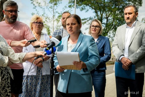 Chodnik przy ul. Unruga, dzień, konferencja prasowa, na środku przemawia Aleksandra Kosiorek, w tle Tomasz Augustyniak, Agnieszka Tokarska, Teresa Bysewska, Łukasz Strzałkowski, obok dziennikarze i mikrofony