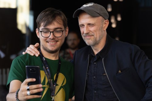 Młody mężczyzna w koszulce wolontariusza FPFF robi sobie zdjęcie telefonem z aktorem Łukaszem Simlatem