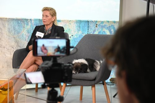 Studio publicystyczne, Ewa Kasprzyk siedzi w fotelu, mówi do mikrofonu, na fotelu obok śpi mały pies. Błękitne tło, sprzęt wideo