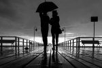 Para idąca po parasolem na molo w Orłowie w momencie przelotnego deszczu oraz przebijającego się przez chmury słońca.
