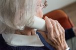 Zdjęcie starszej kobiety z siwymi włosami, która rozmawia przez telefon stacjonarny (słuchawka w dłoni przyłożona do ucha)