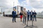 Grupa ludzi na parkingu przy GCS. Prezydent Wojciech Szczurek przemawia do mikrofonów. W tle ciężarówka z naczepą i logo Gdyni na tle ukraińskiej flagi