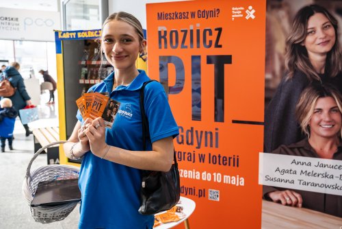 Hol Centrum Batory, kobieta w niebieskiej koszulce trzyma ulotki akcji Rozlicz PIT w Gdyni, w tle ekspozycja kampanii