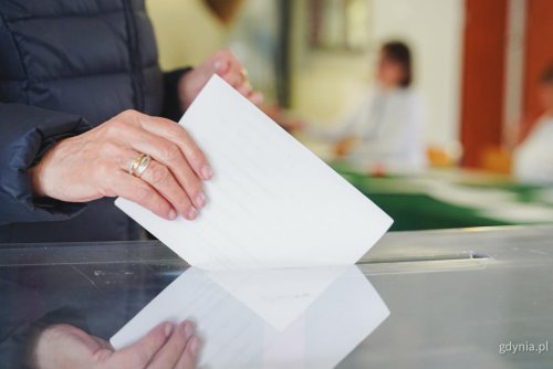 Lokal wyborczy, urna, kobieca dłoń wrzuca do urny białą kartkę