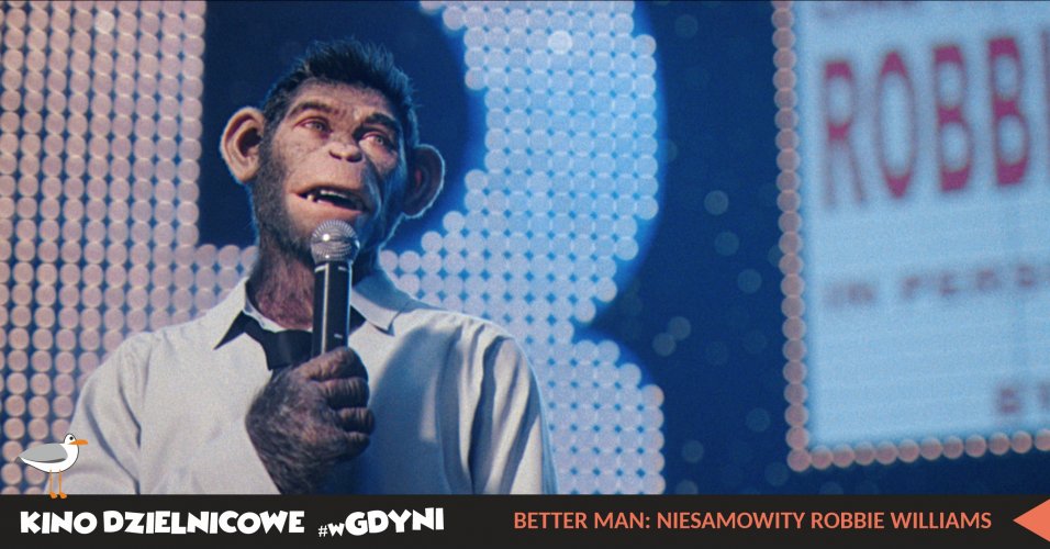 Kadr z filmu Better Man: Niesamowity Robbie Williams”. Szumpans w koszuli i krawacie stoi na scenie z mikrofonem.