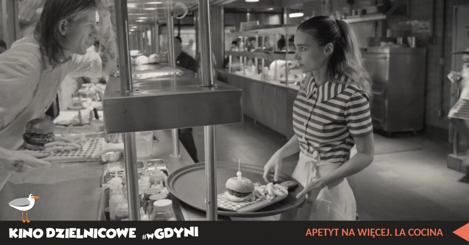 Kadr z filmu „Apetyt na więcej. La Cocina”. Czarno-białe zdjęcie. Amerykański bar, kucharz patrzy na kelnerkę z hamburgerem na tacy.