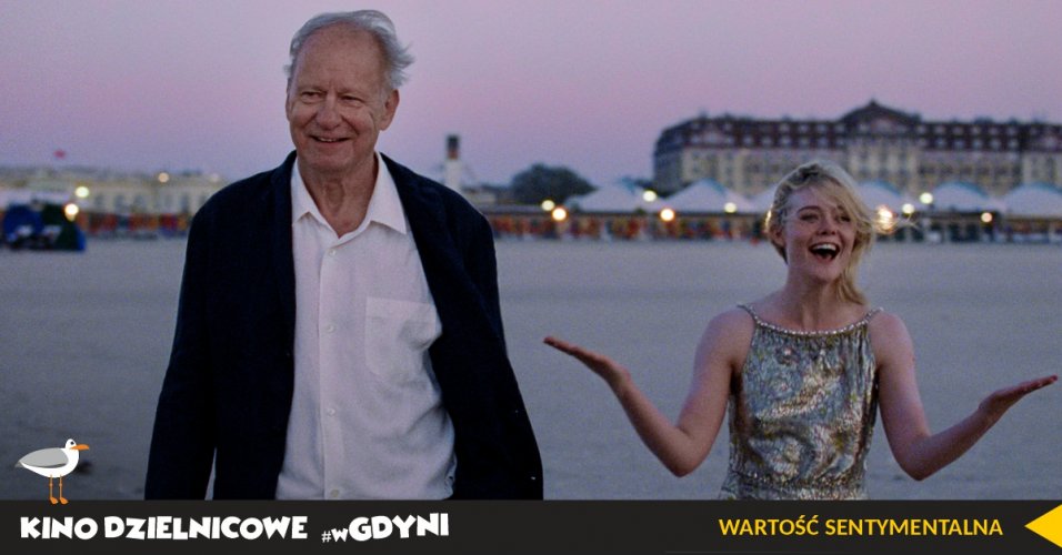 Kadr z filmu "Wartość Sentymantalna". Usmiechnięci starszy mężczyzna i kobieta w błyszczącej sukni na tle hotelu na plaży. 