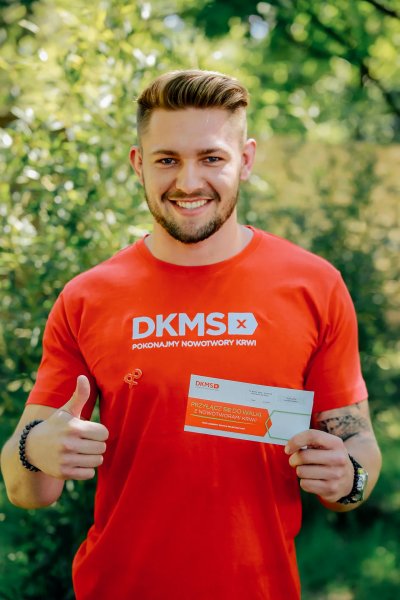 Mężczyzna w czerwonej koszulce DKMS i pakietem rejestracyjnym