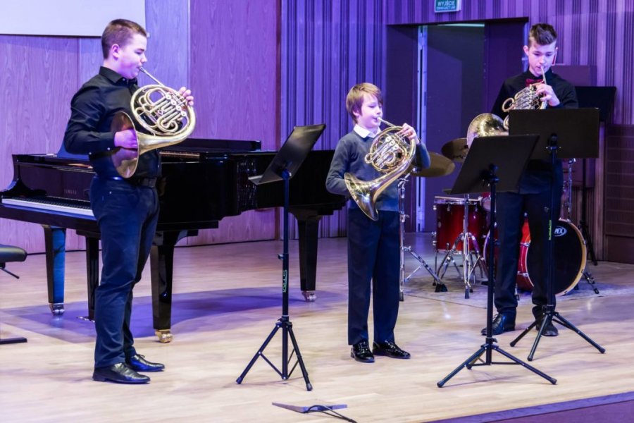 Troja uczniów podczas gry na instrumentach na scenie