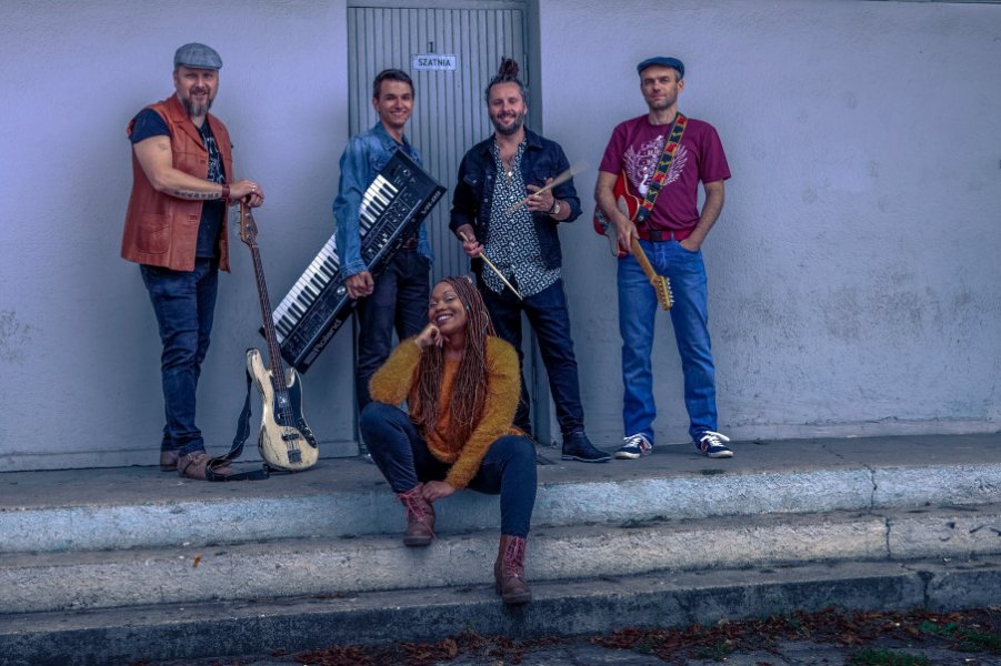 Grupa muzyków stojąca przy budynku.