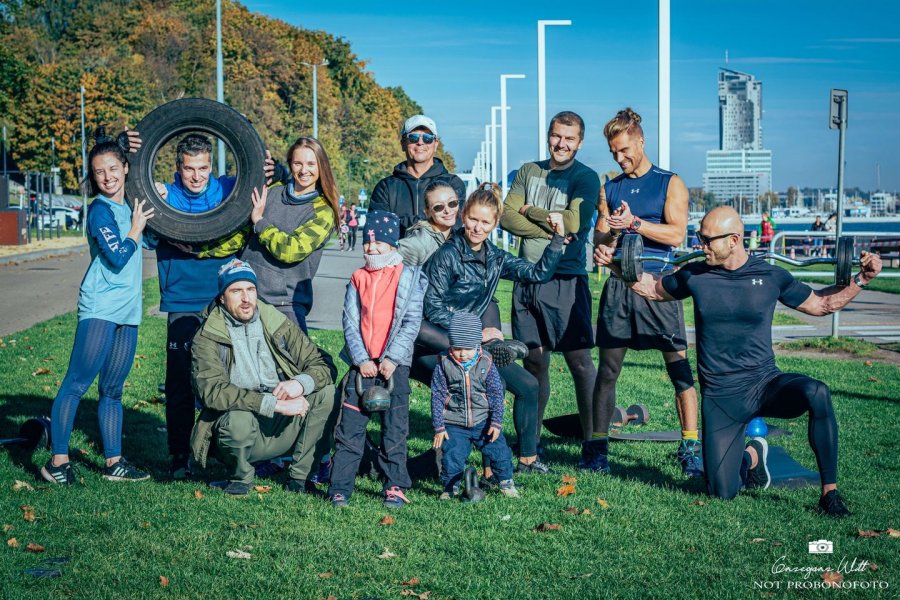 Grupa sportowców pozująca na zielonej trawie. W tle bulwar i morze.