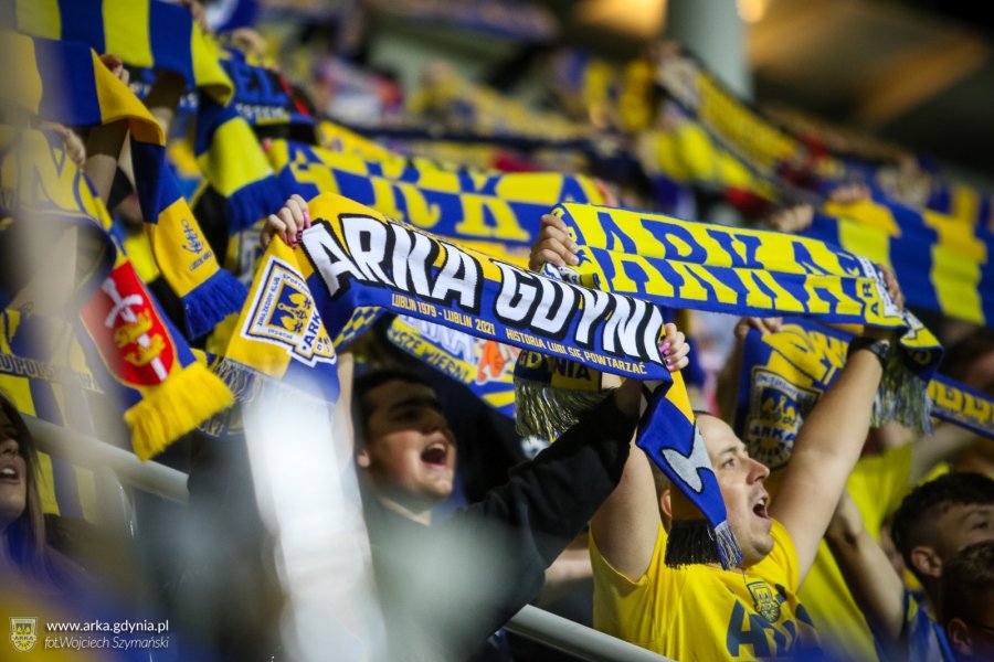 Kibice na trybunach trzymający szaliki z napisem Arka Gdynia