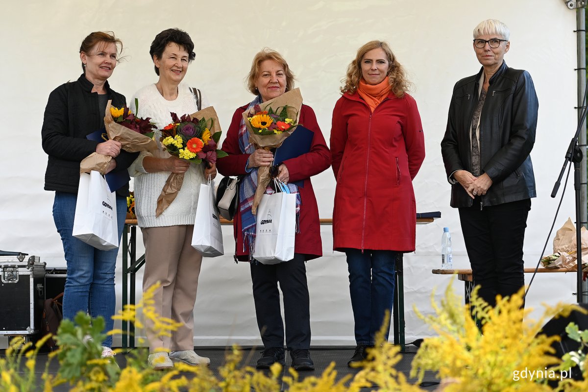 Pięć kobiet na scenie pozuje do zdjęcia. Cztery z nich trzymają nagrody i kwiaty.