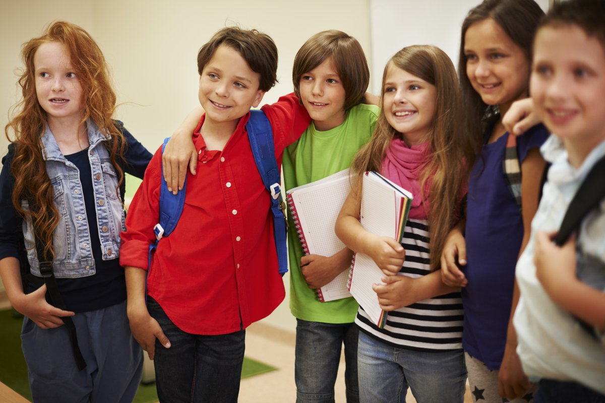 Na zdjęciu grupa dzieci w wieku szkolnym, które stoją na korytarzu w szkole. Dzieci są uśmiechnięte, kolorowo ubrane. Źródło: Freepik.com