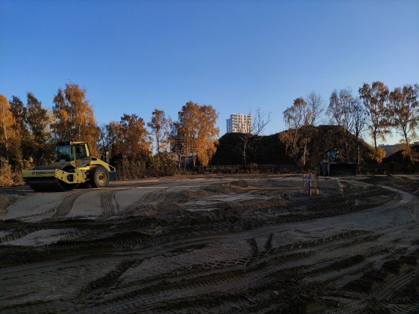Plac budowy, ziemia. Koparka na placu, w tle budynki