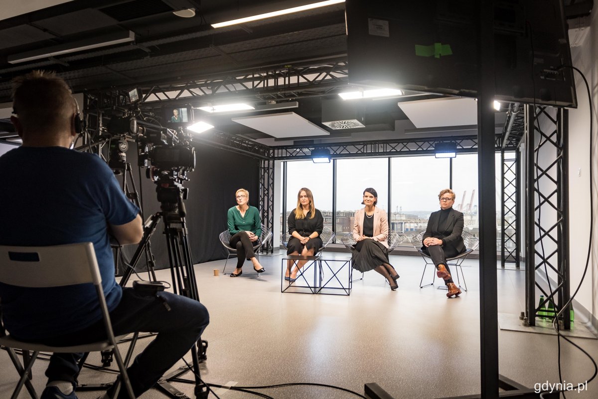 Studio nagraniowe. Cztery kobiety na krzesłach w studio. W tle okna i port w Gdyni. Widoczny operator kamery