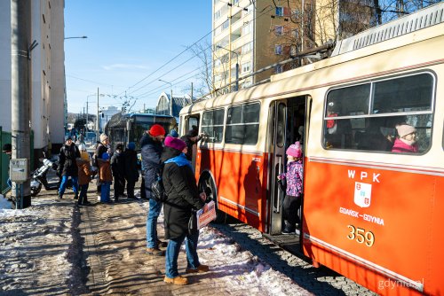 Ulica Wójta Radtkego, zima, zabytkowy, czerwony trolejbus, do którego wsiadają ludzie, z tyłu kolejny trolejbus
