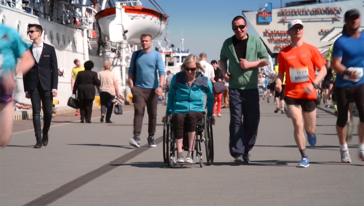 Kadr ze spotu Miasto równych szans przedstawia spacerowiczów, biegaczy i osobę poruszającą się na wózku na gdyńskim nabrzeżu