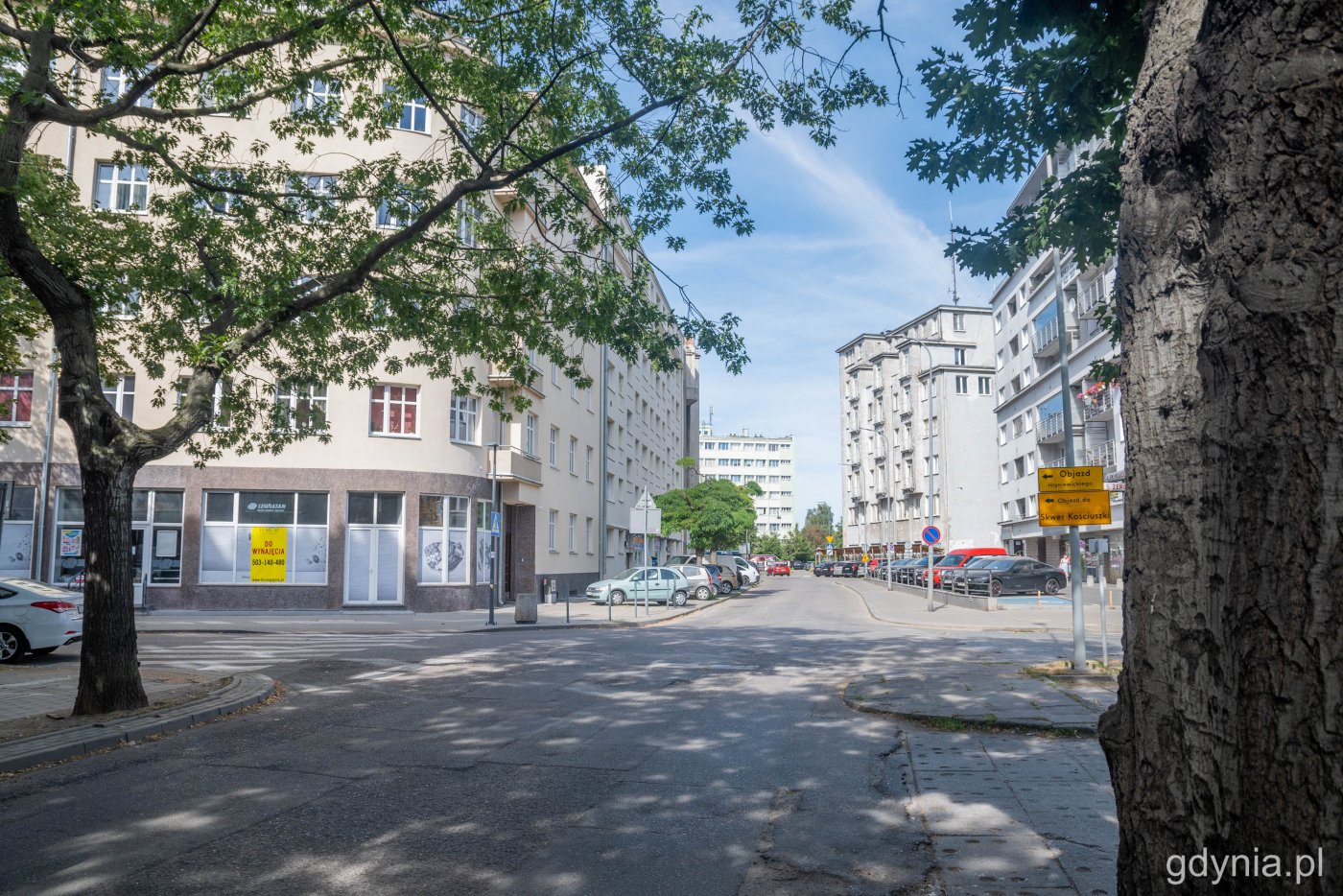 Ulica świętego Wojciecha w Gdyni. Widoczne drzewa, budynki, zaparkowane samochody. Letni dzień
