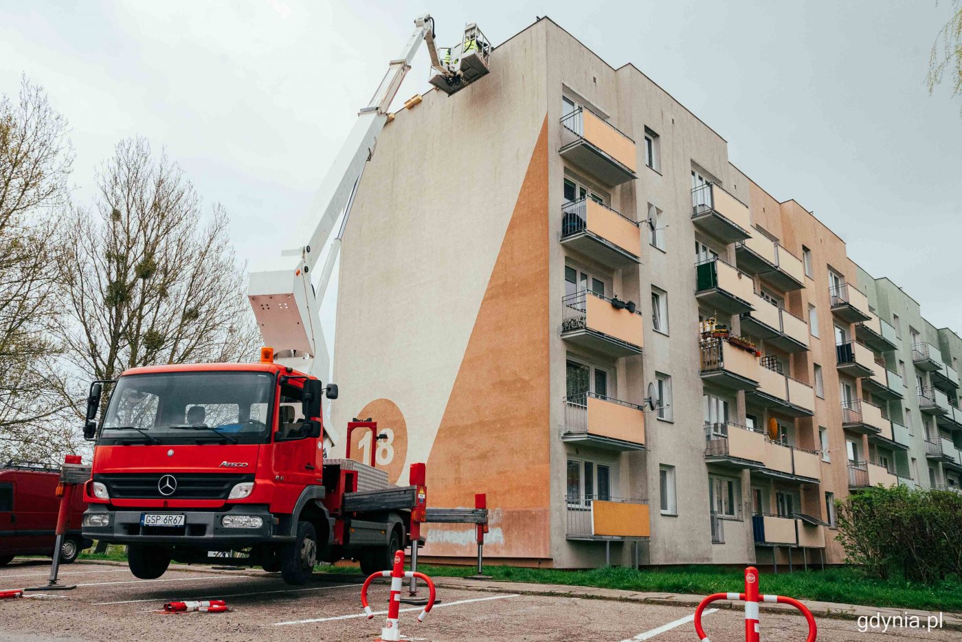 Witomino, ściana bloku mieszkalnego z numerem 18, parking. Ciężarówka z podnośnikiem trzyma pracowników przy szczycie ściany.