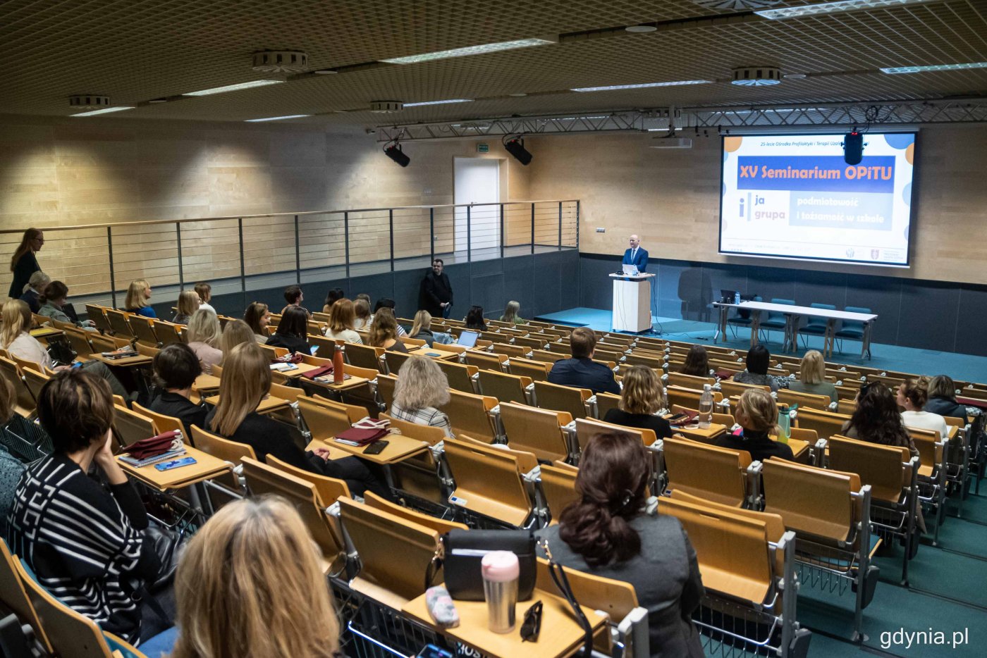 Sala Morska w PPNT Gdynia, ludzie na widowni, ekran na środku, Bartosz Bartoszewicz przemawia przy katedrze