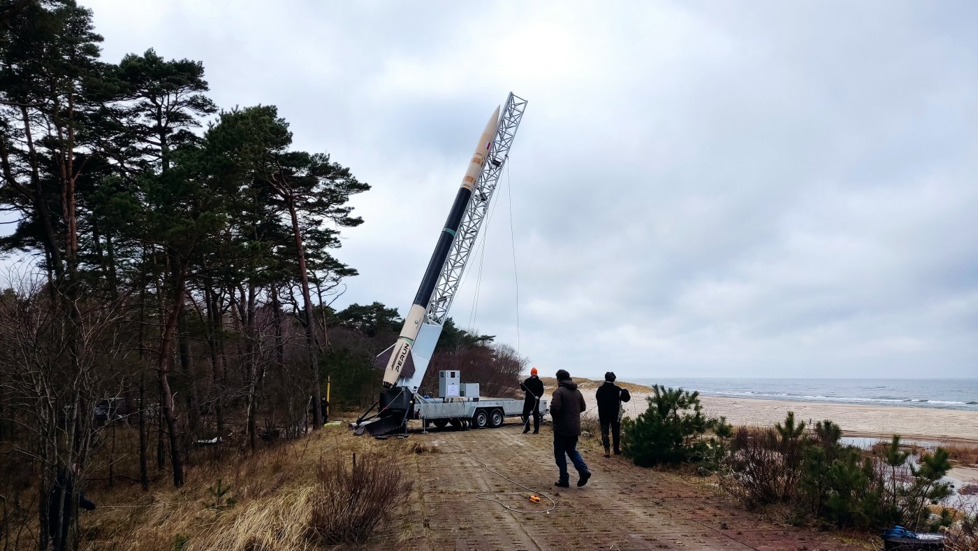 Poligon, skarpa nad plażą, morze, rakieta kosmiczna rozstawiona na pojeździe, obok kilka osób, jesień/zima