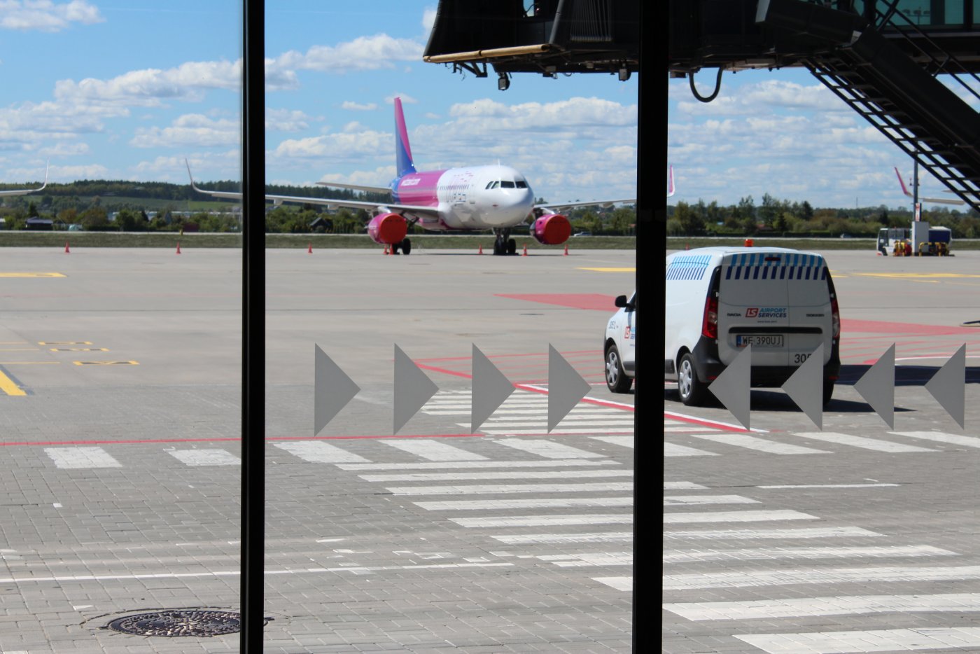 Zdjęcie z Lotniska im. Lecha Wałęsy w Gdańsku. Z okna widać pas startowy, samolot oraz samochód.