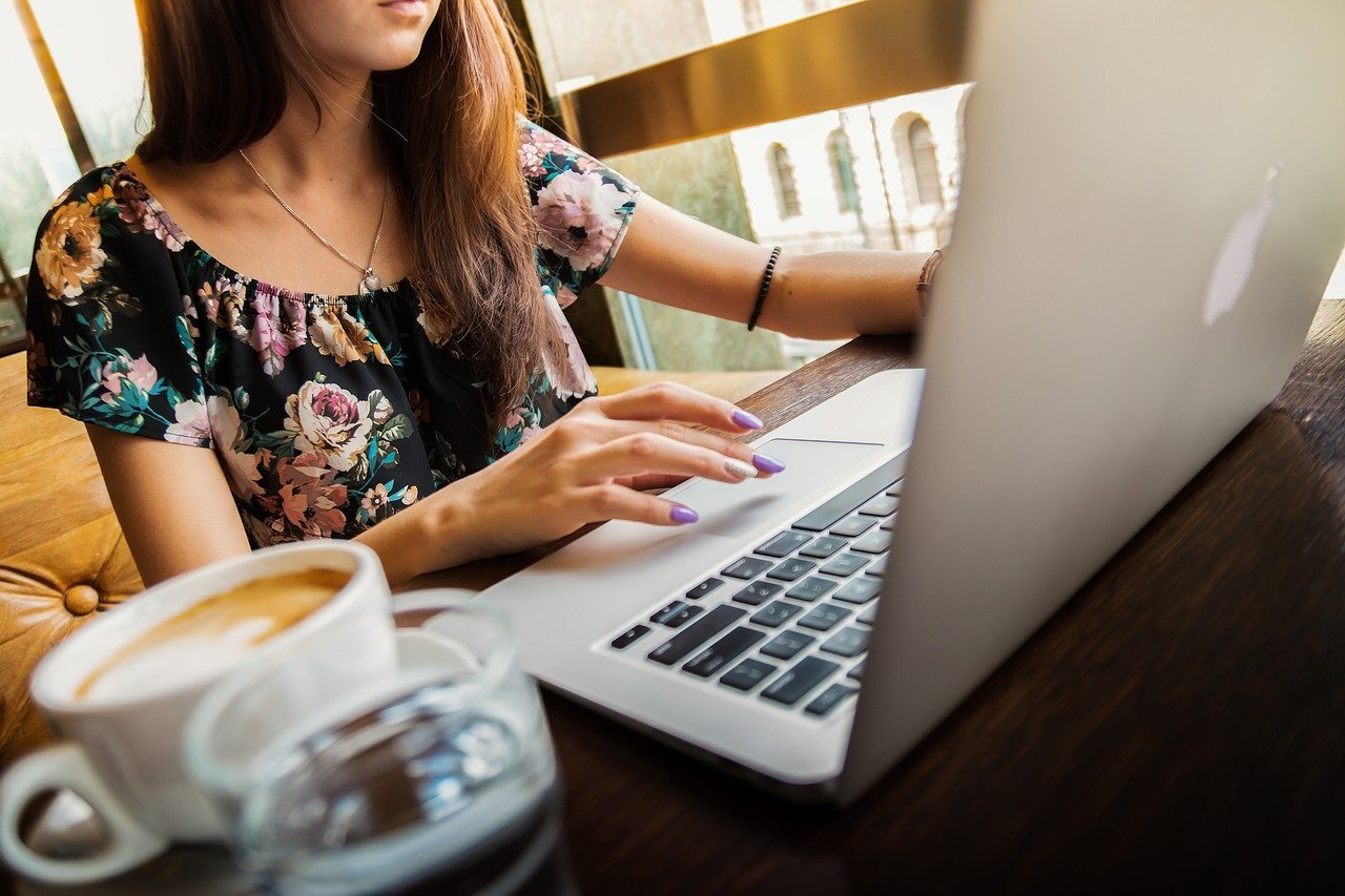 Kobieta przy biurku pracuje na laptopie. Widoczny kubek z kawą