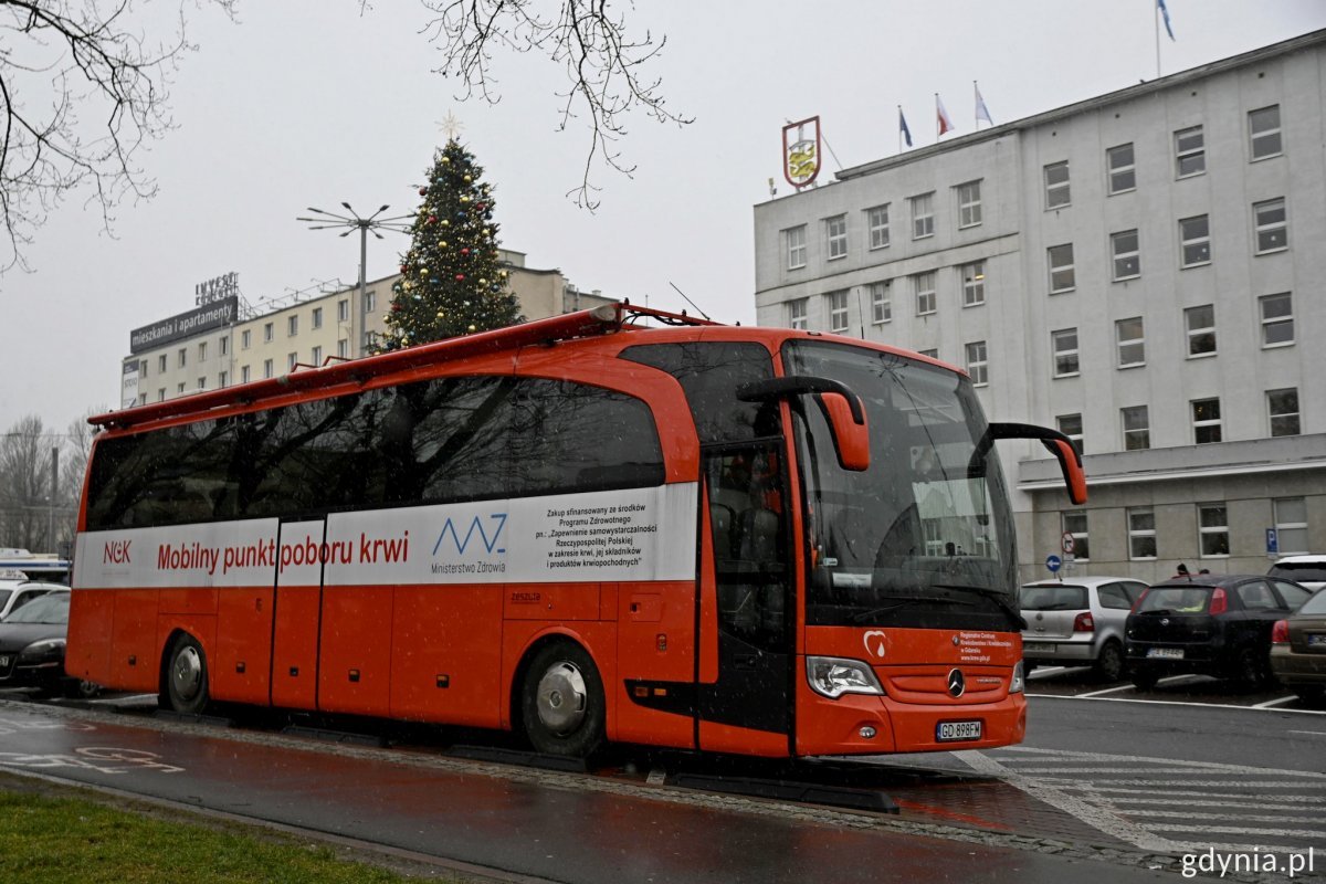 Krwiobus zaparkowany na poboczu, w tle Urząd Miasta Gdyni i parking samochodowy