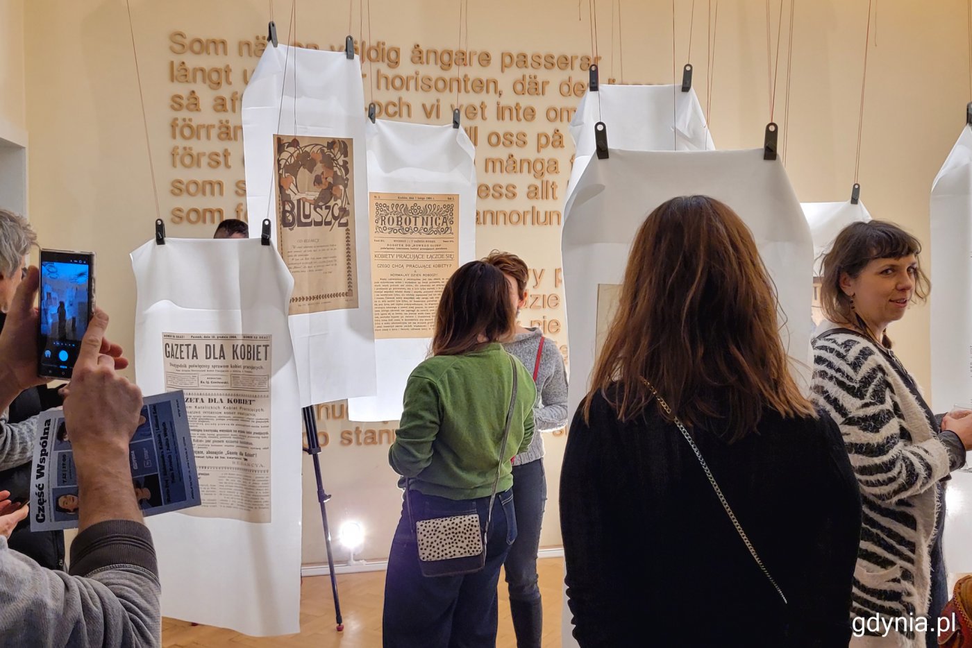 Wystawa w Konsulacie Kultury, ludzie, wiszące elementy wystawy - strony z gazet