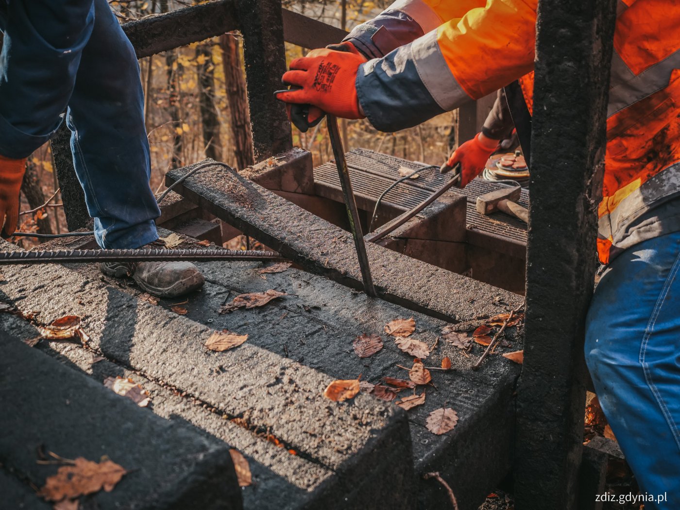 Spalone schody na Babich Dołach, robotnicy w pomarańczowych kamizelkach, jeden z nich ma łom w ręku, próbuje oderwać spaloną poręcz