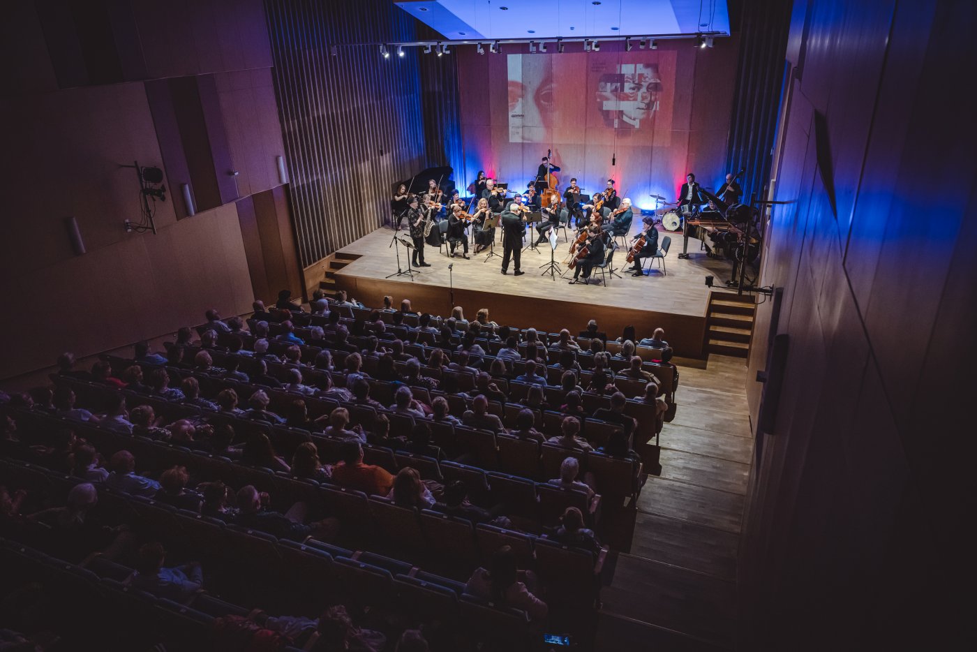 Sala koncertowa szkoły muzycznej w Gdyni. Na widowni ludzie, na scenie kilkunastoosobowa orkiestra z instrumentami i dyrygentem.