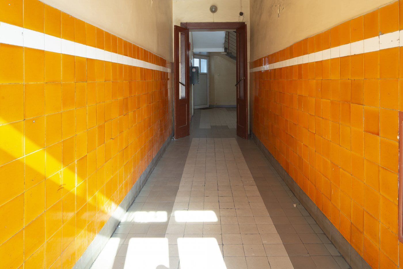 Strefa wejściowa w kamienicy przy Skwerze Kościuszki 14, dolne partie ścian wykończone ceramicznymi pomarańczowymi płytkami z wykończeniem z białym paskiem.