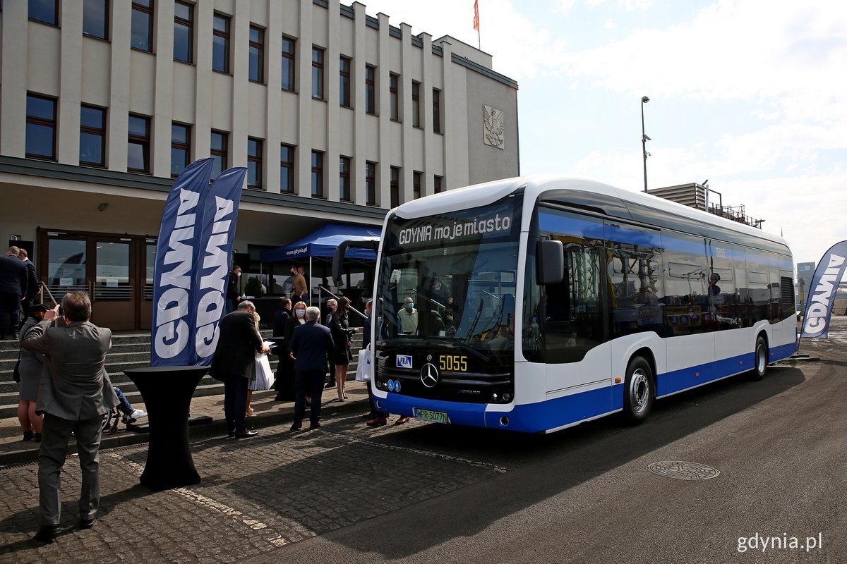 Biało-niebieski autobus marki Mercedes-Benz stojący przed Muzeum Emigracji. Na schodach ludzie.