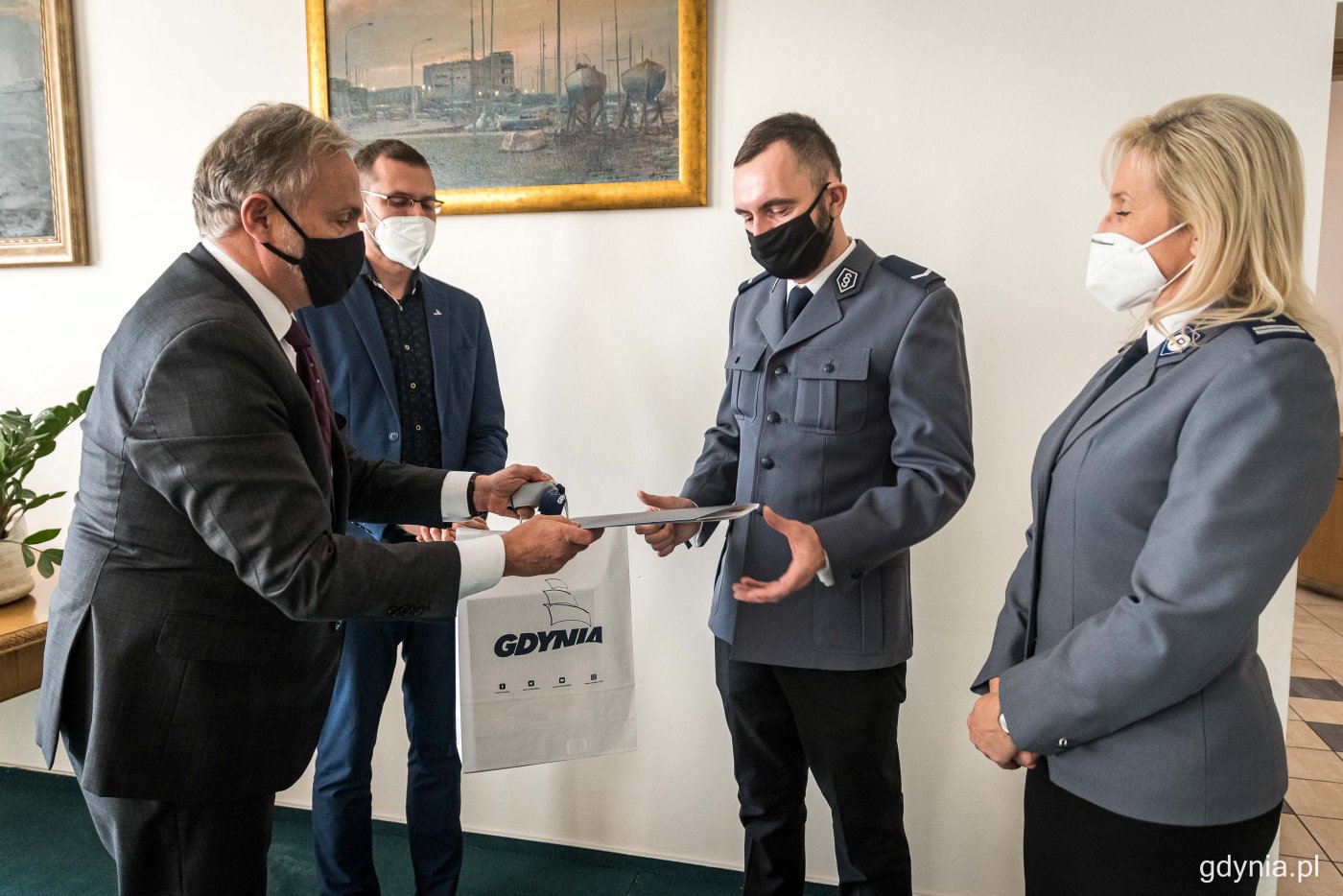 Lechosław Dzierżak, Wojciech Szczurek i dwoje policjantów - mężczyzna i kobieta - w sali Urzędu Stanu Cywilnego. Policjant odbiera z rąk Wojciecha Szczurka list z podziękowaniami i torbę z logotypem Gdyni.