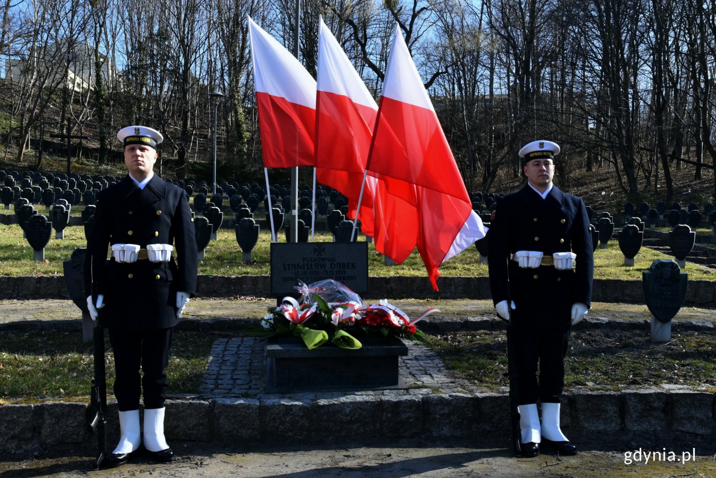 na zdjęciu trzy biało-czerwone flagi powiewające na wietrze i warta honorowa