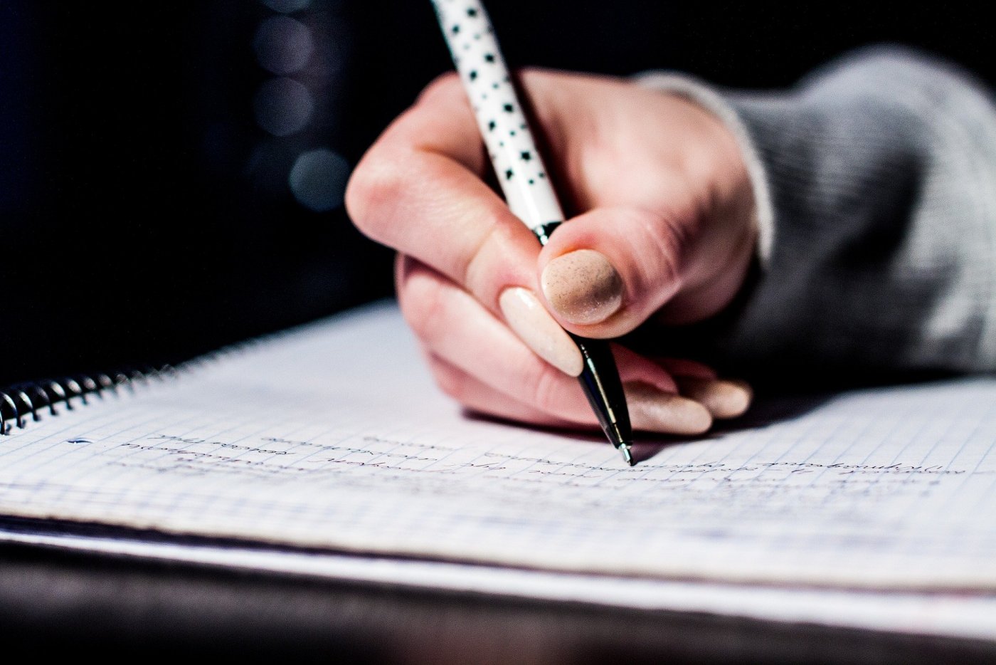 Kobieca dłoń trzymająca biały długopis w czarne gwiazdki i pisząca w zeszycie z notatkami