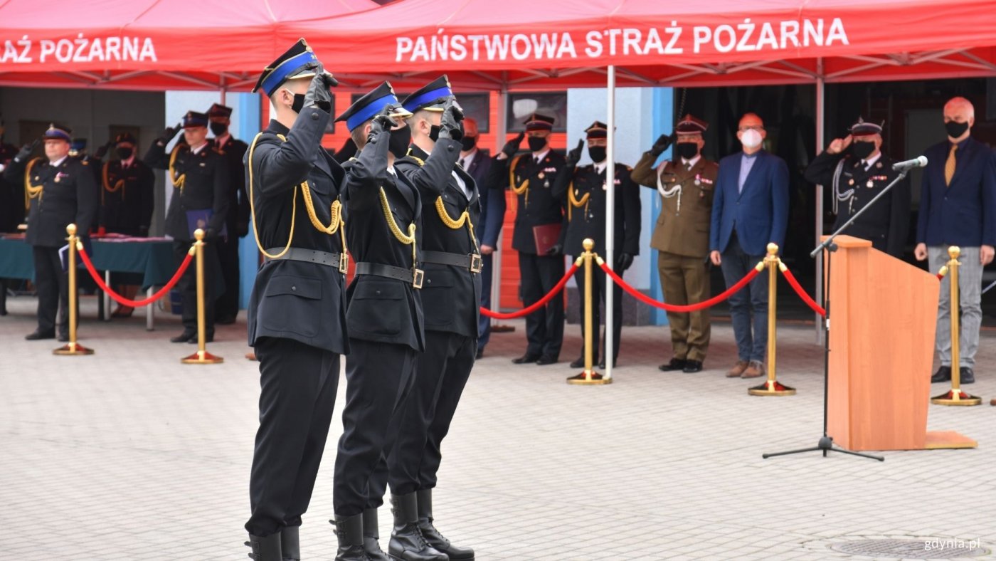 Obchody Dnia Strażaka w Gdyni w Jednostce Ratowniczo-Gaśniczej nr 2, fot. Magda Śliżewska. Goście i odświętnie ubrani strażacy salutują w czasie podnoszenia polskiej flagi.