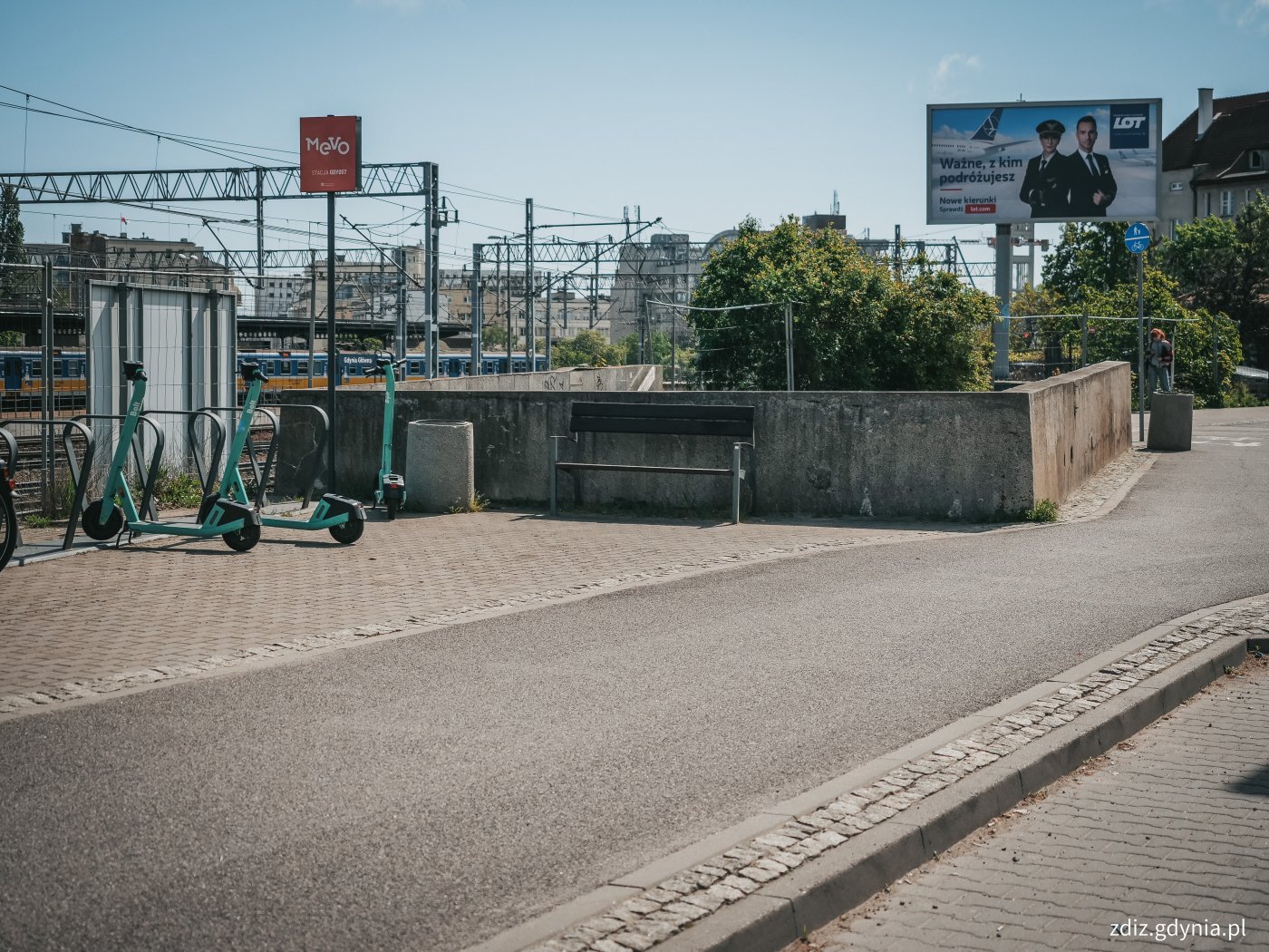 widok na chodnik i ścieżkę rowerową, widoczne zaparkowane hulajnogi oraz ławka