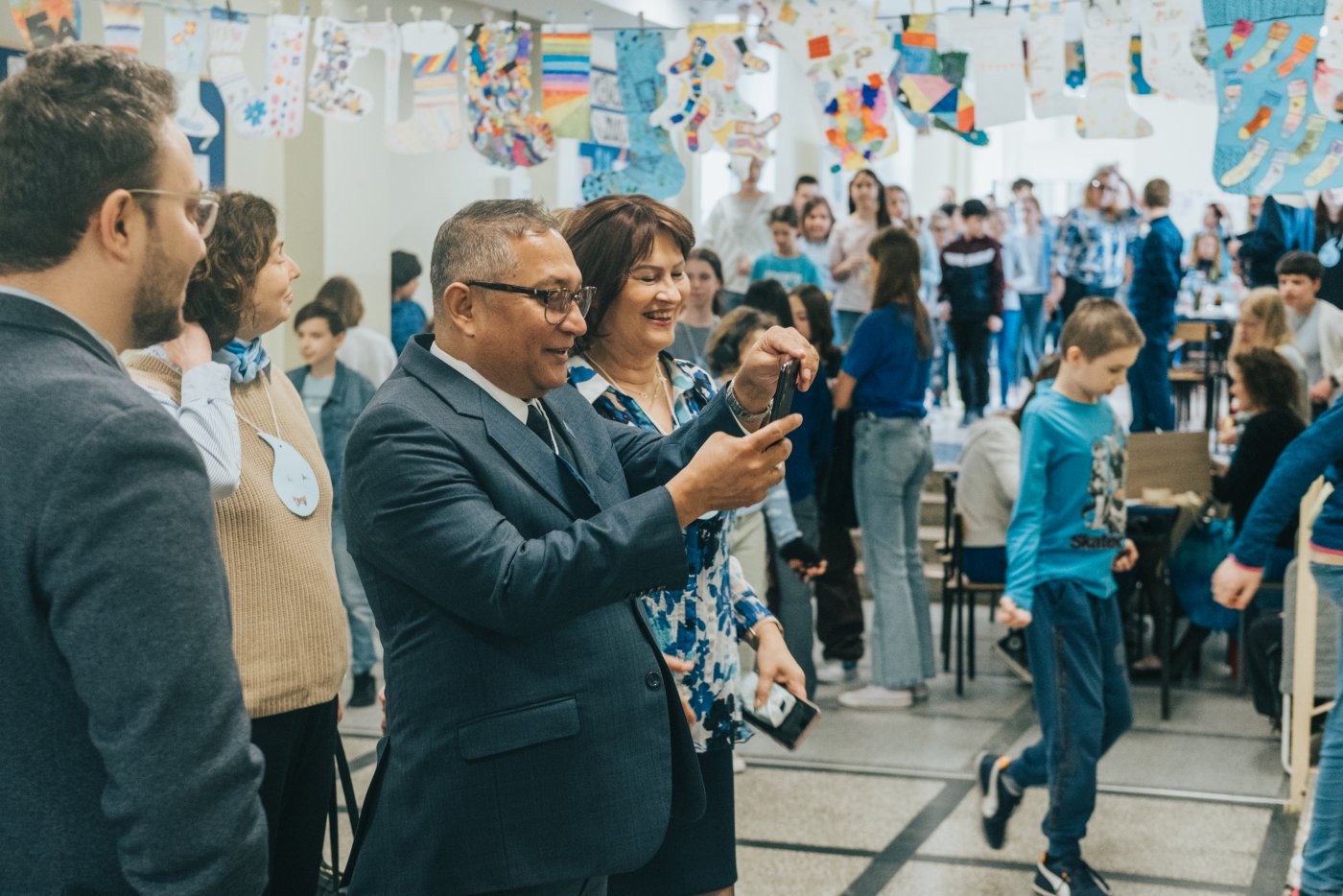 Przedstawiciel UNICEF i dyrektor szkoły wśród dzieci. W tle niebieskie dekoracje