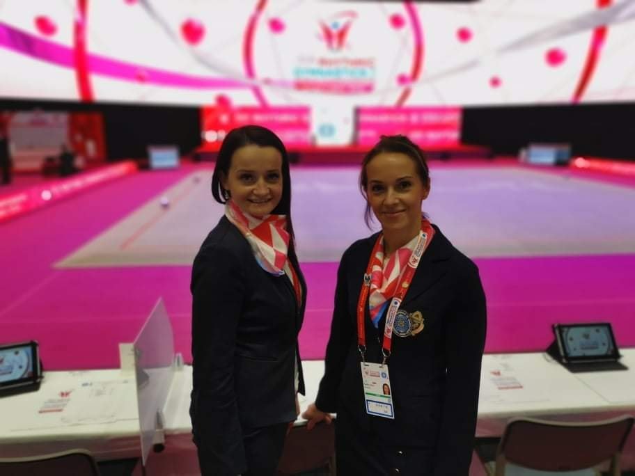 Dwie sędziny w oficjalnych strojach, w tle hala sportowa.